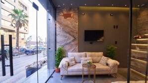 A modern living room with a beige sofa, a round gold side table, and a marble-patterned wall. - Gold's Pyramids Hotel (Giza)