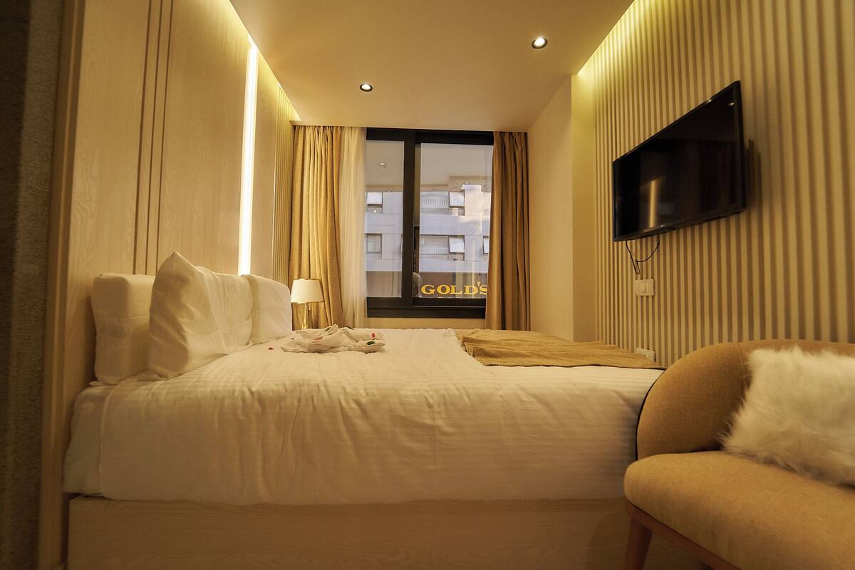 A hotel room with a bed, a TV mounted on the wall, and a view of the city through the window.