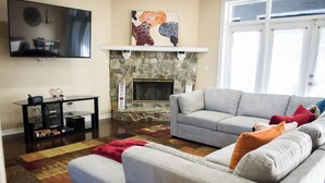 A living room with a stone fireplace, a grey sofa set, a flat-screen TV, and a coffee table. - Relax in Heated Saltwater Pool w/ Screened Lanai (Lakeland)