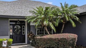 A residential house with a dark grey exterior, a black front door with a wreath, a well-maintained hedge, and a palm tree. - Relax in Heated Saltwater Pool w/ Screened Lanai (Lakeland)