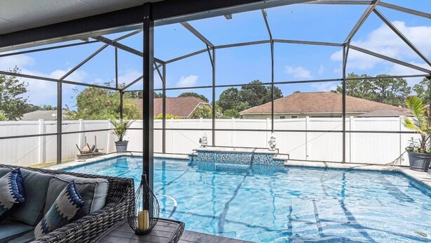 A covered outdoor swimming pool with a view of the backyard, a wicker sofa, and a potted plant. - Relax in Heated Saltwater Pool w/ Screened Lanai (Lakeland)