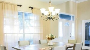 A dining room with a rectangular table surrounded by six chairs, a chandelier, and a vase with flowers on the table. - Relax in Heated Saltwater Pool w/ Screened Lanai (Lakeland)