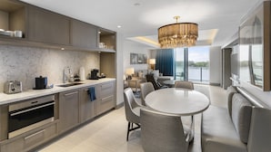 A modern kitchen with built-in appliances, a dining area with a round table and chairs, and a large window offering a view of the city.