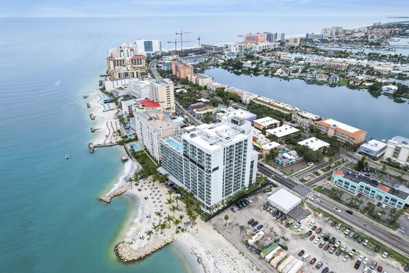 Vista aérea de una ciudad costera con un hotel frente a la playa, un puerto deportivo y edificios residenciales circundantes.