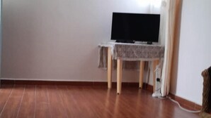 Une pièce avec un plancher en bois, un téléviseur à écran plat posé sur une table et une fenêtre avec des rideaux.