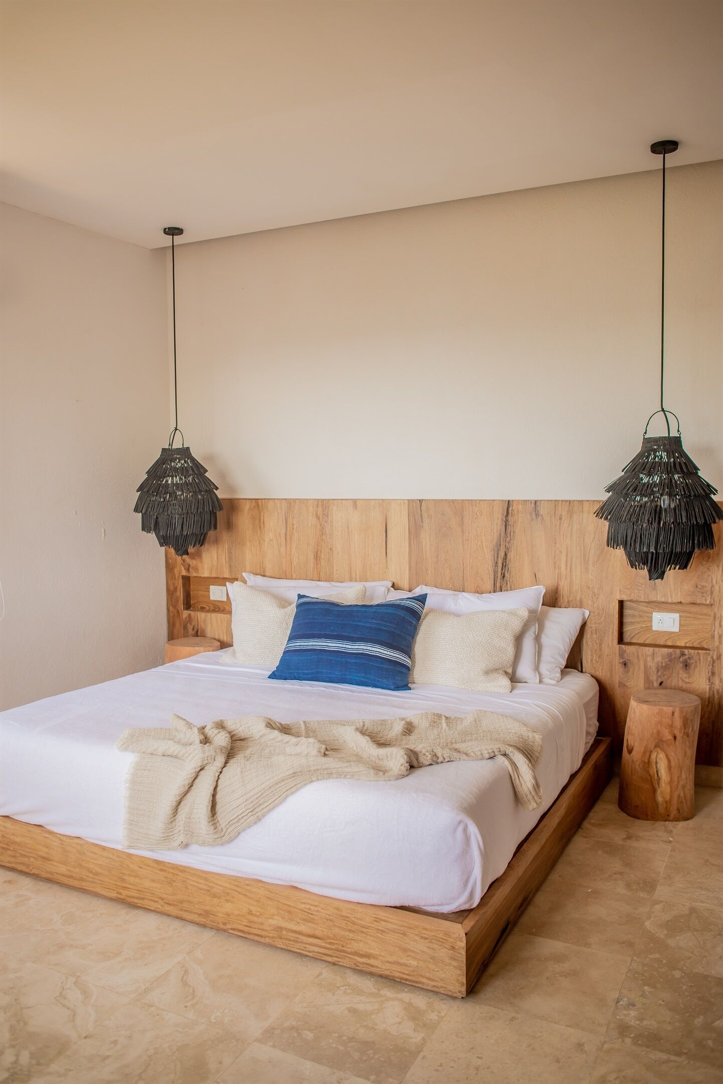 Un dormitorio moderno con cabecera de madera, una cama grande con ropa de cama blanca y dos lámparas colgantes.