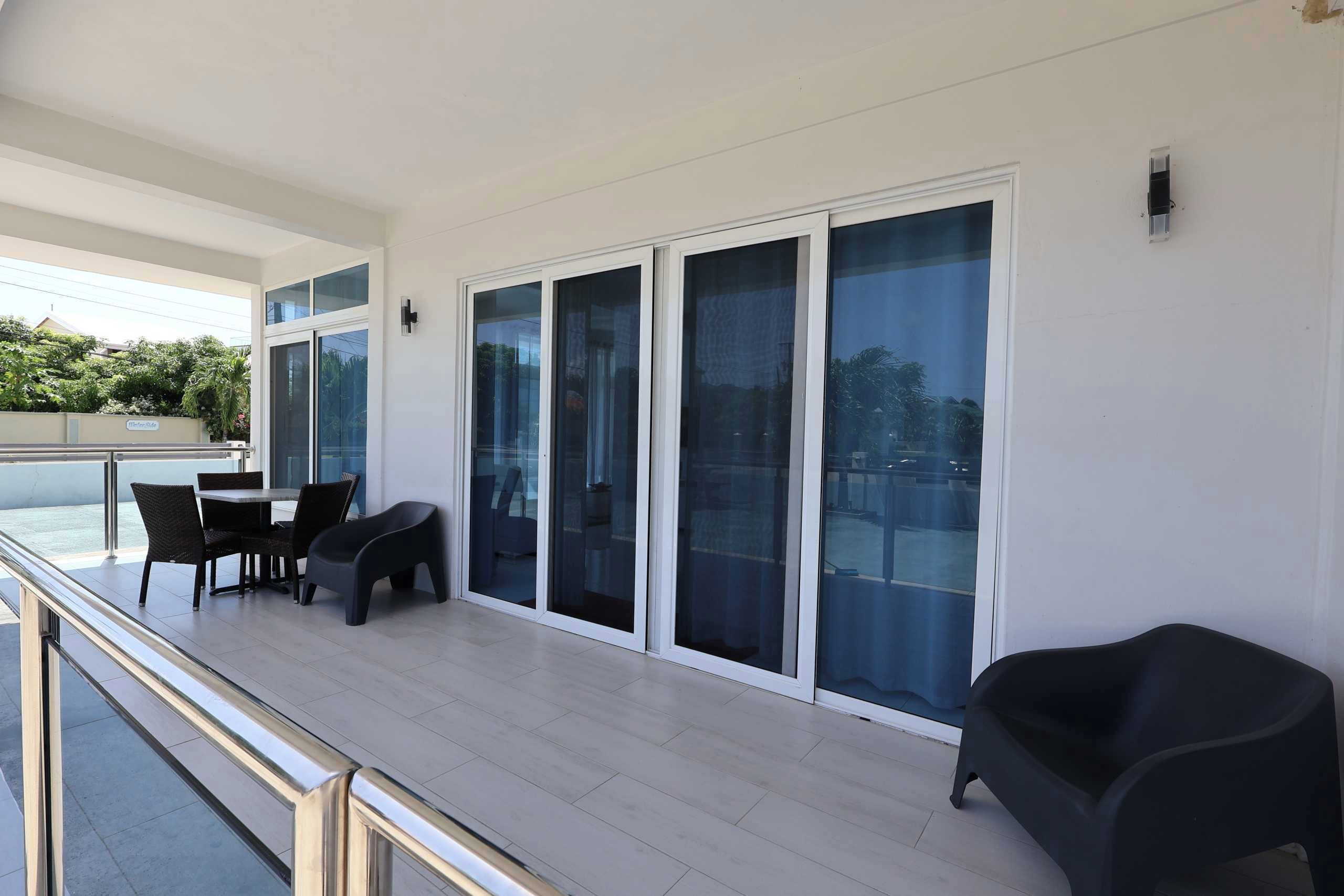 A balcony with a glass door, a table with chairs, and a black chair.