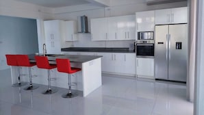 A modern kitchen with white cabinets, a stainless steel refrigerator, and a central island with red bar stools. - PÀRIS Villas 2BD Villa Rodney Bay (Gros Islet)