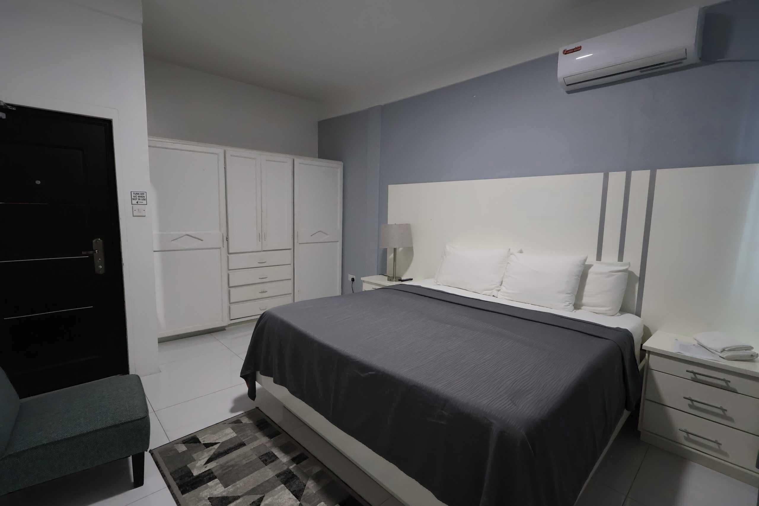A bedroom with a bed, bedside tables, a wardrobe, and an air conditioning unit.