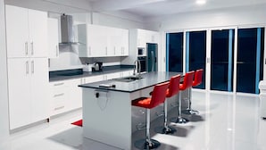 A modern kitchen with white cabinets, a central island with a glass top, and red bar stools. - PÀRIS Villas 2BD Villa Rodney Bay (Gros Islet)