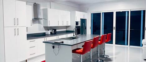 Una cocina moderna con armarios blancos, una isla central con encimera de vidrio y taburetes de bar rojos.