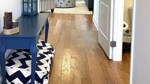 Un couloir avec une table bleue et des poufs à motifs, un ventilateur de plafond, et une vue sur un salon avec des meubles à rayures et un tapis.