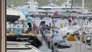 Een jachthaven met aangemeerde boten, een persoon op een boot en een steiger met mensen en apparatuur.