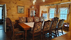 Uma sala de jantar com painéis de madeira, uma mesa grande e cadeiras elaboradas, um armário com portas de vidro e um letreiro de boas-vindas.