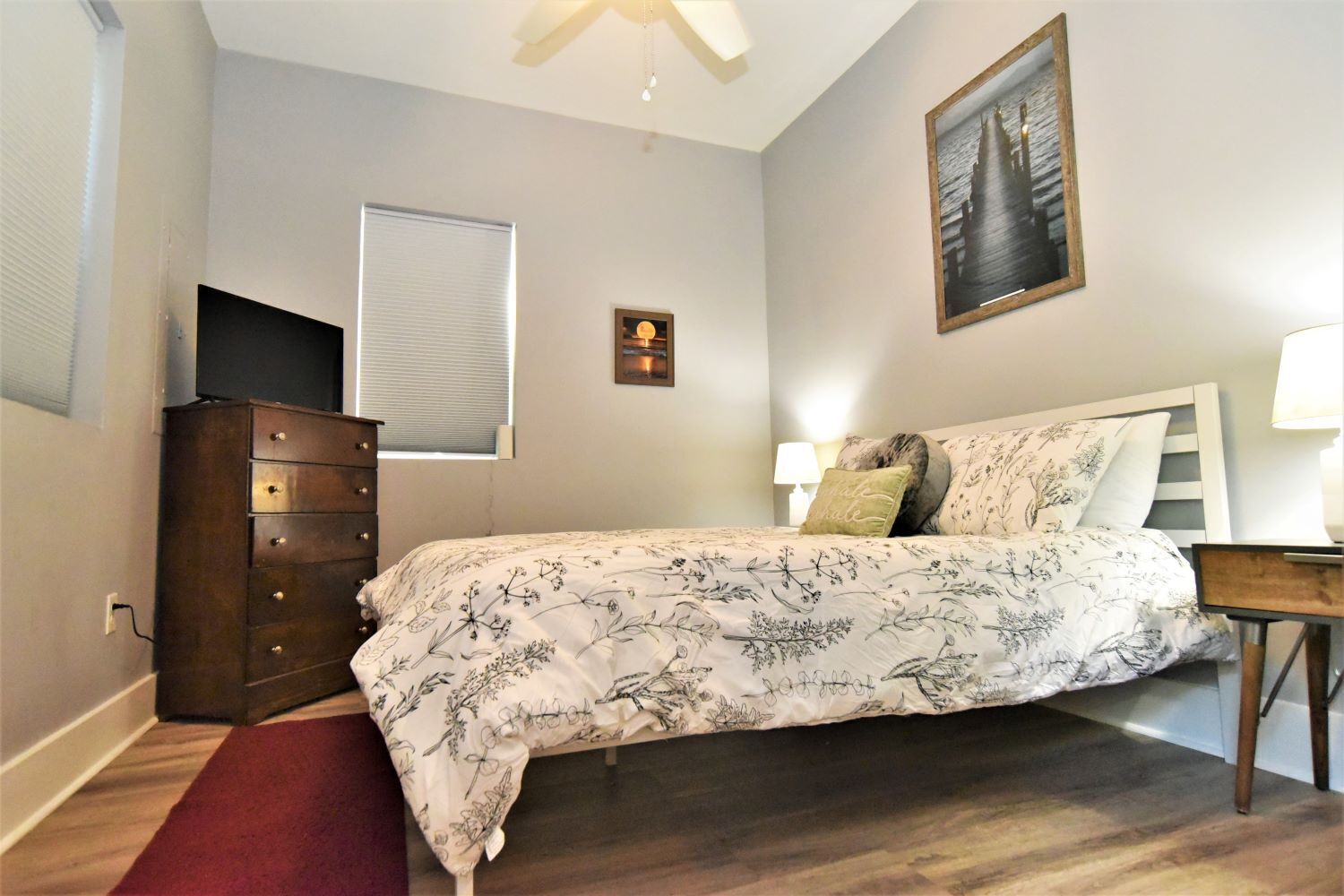 A bedroom with a bed, dresser, window, and artwork on the wall.
