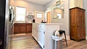 A modern kitchen with a stainless steel refrigerator, white cabinets, a microwave, and a wooden cabinet. - Teal Door Inn-With Fire Pit! (Charleston)