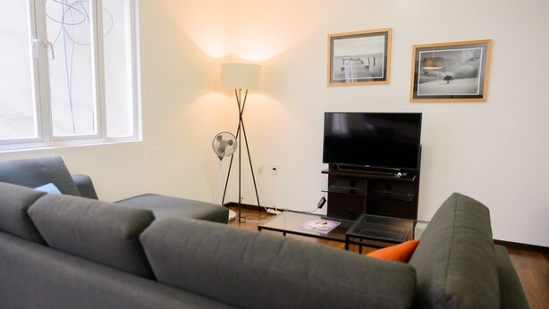 Ett vardagsrum med en soffa, en tv, en lampa och två inramade tavlor på väggen.