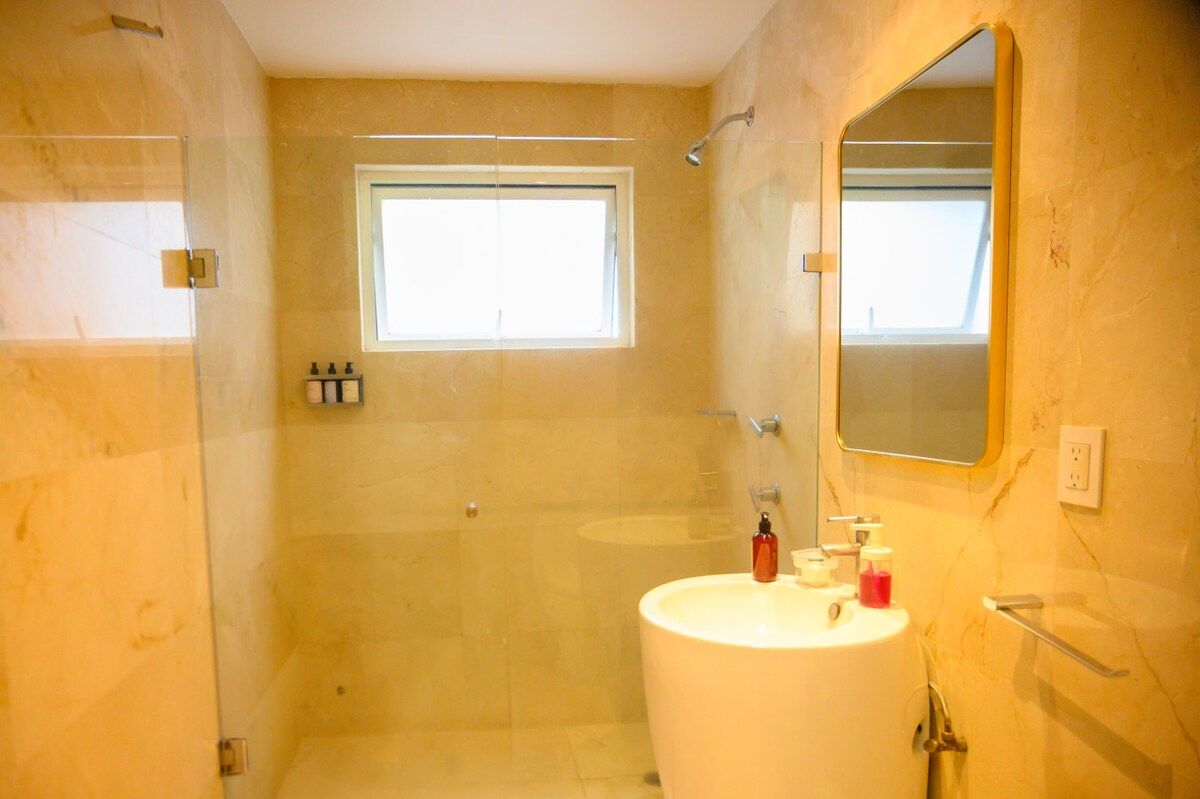 Ein Badezimmer mit Dusche, Waschbecken, Spiegel und Fenster.