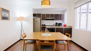 En matplats med ett träbord och stolar, en hängande lampa och ett kök i bakgrunden.