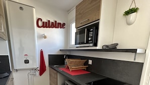 Een compacte keuken met een ingebouwde magnetron, een vaatwasser en een rode handdoek aan de muur.