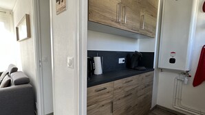 Een kleine keuken met houten kastjes, een zwart aanrecht en een witte koelkast.