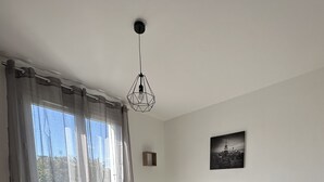 Een slaapkamer met een groot bed, een hanglamp, een stadsgezicht schilderij en een klein rond tafeltje met een lamp.
