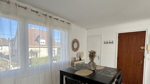 Een eetruimte met een zwarte tafel en stoelen, een houten vloer en een uitzicht door grote ramen.