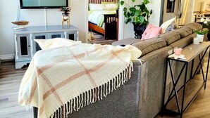 Ett modernt vardagsrum med en grå soffa, en tv, en takfläkt och ett köksutrymme som syns genom en öppen dörr.