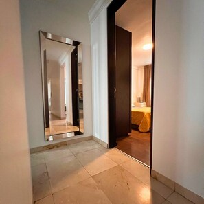 Un couloir avec un grand miroir, une porte donnant sur une pièce et un sol carrelé.