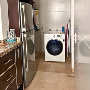 Une cuisine compacte équipée d’un réfrigérateur, d’un lave-linge et d’un plan de travail sur lequel sont posées des bouteilles d’eau.