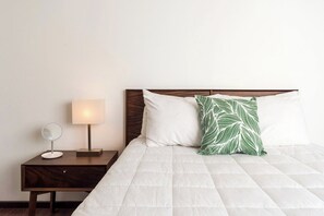 A neatly made bed with a white duvet, a wooden headboard, and a green leaf-patterned pillow.