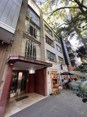 A multi-story building with a covered entrance, outdoor seating area, and visible balconies.