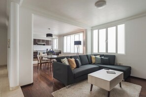 A modern living room with a dark-colored sofa, a white coffee table, and a dining area with a table and chairs. - Condesa Residence Campeche 7 (Ciudad de México)