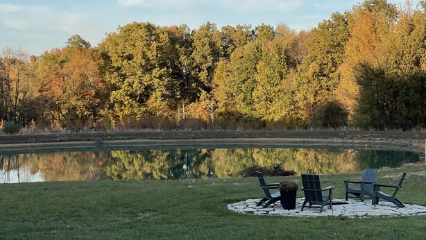 A tranquil outdoor setting with a gravel path leading to a grassy area with two Adirondack chairs and a picnic table.
