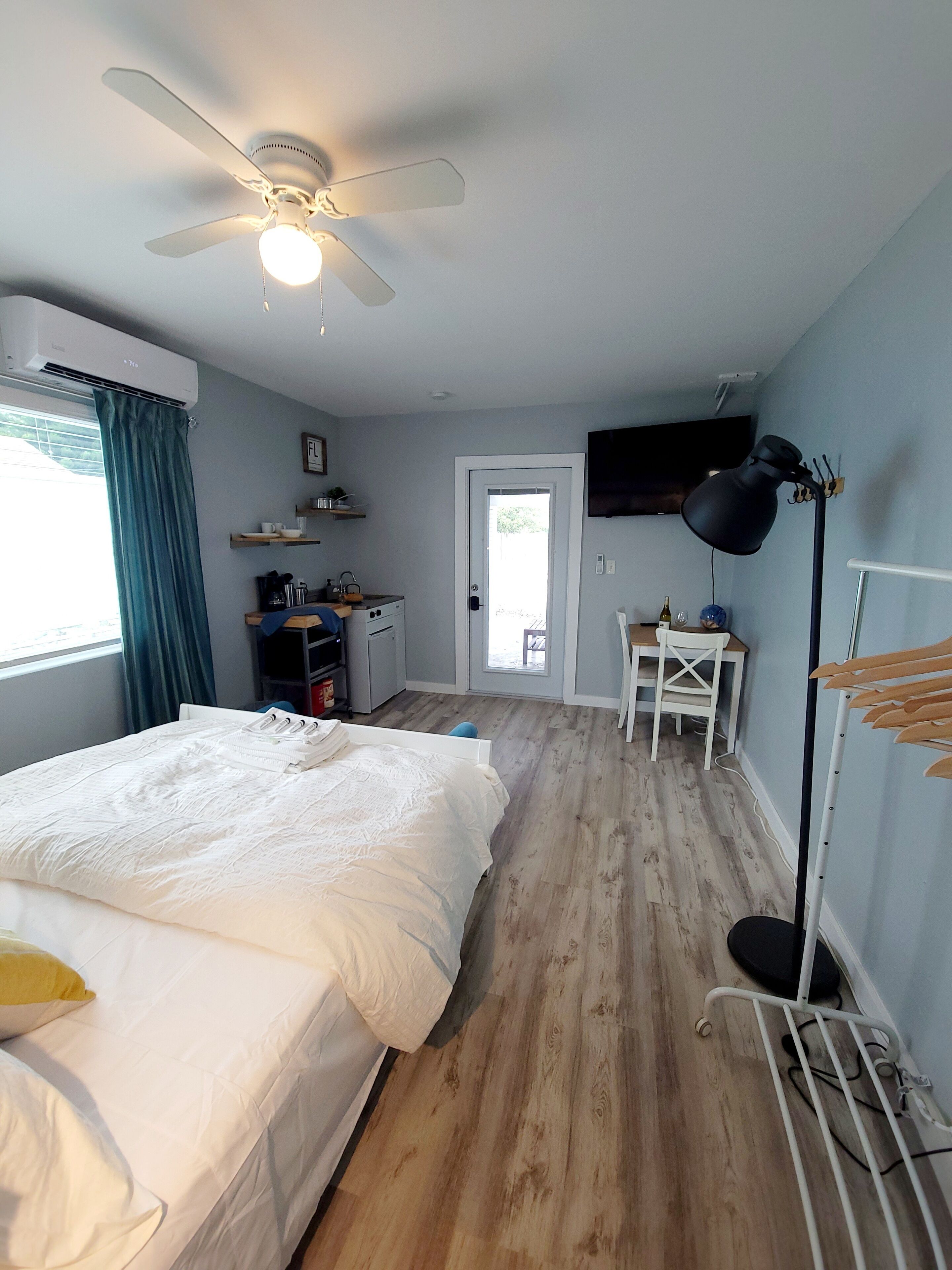 A bedroom with a bed, a ceiling fan, a TV, a desk, and a chair.