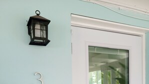 Une porte avec un panneau de verre, une plaque portant le chiffre « 3 », un interrupteur et une lanterne noire fixée au mur.