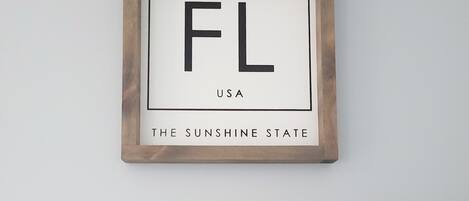 A framed sign with "FL" and "USA" on a wall, a metal pot, a white bowl, and a small potted plant.