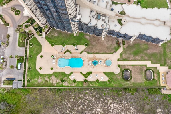 An aerial view of a hotel with a central swimming pool, multiple outdoor seating areas, and a landscaped garden.