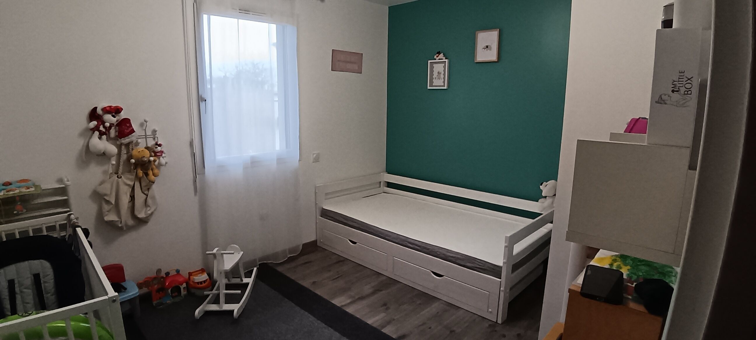 A child's room with a bed, a crib, toys, and a window.