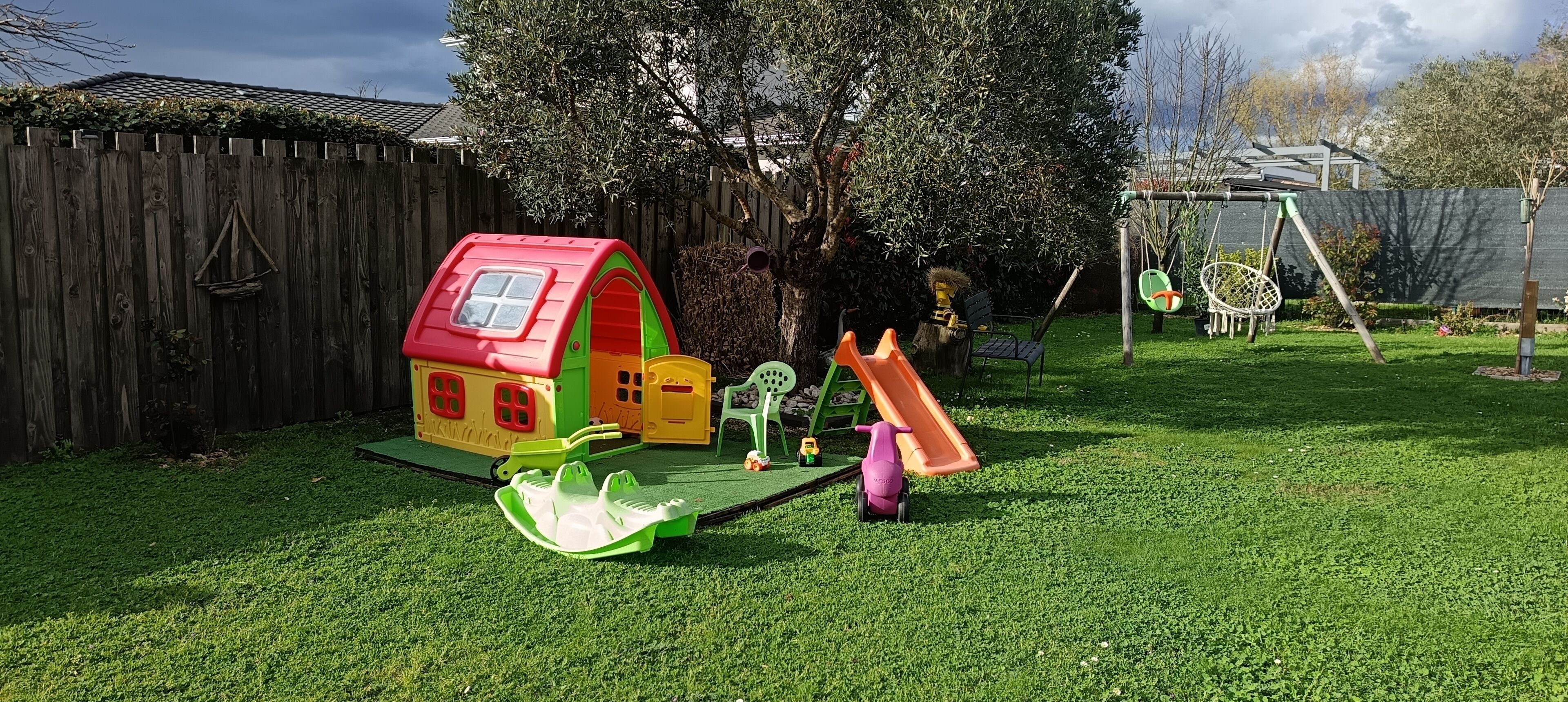 A fenced backyard with a playhouse, a slide, and a swing set.