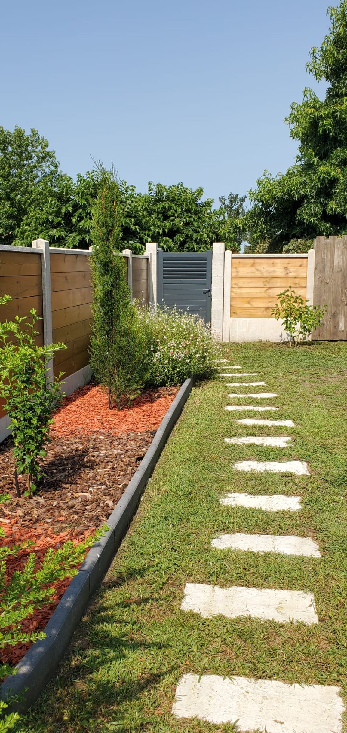 A garden pathway with stepping stones leading to a wooden fence.
