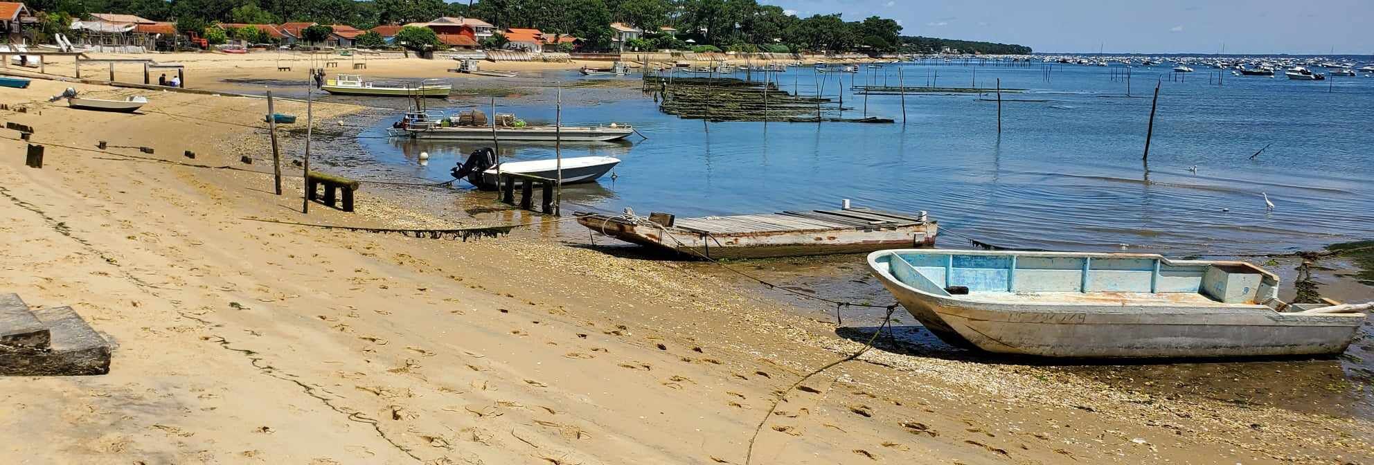 A beach with boats, a sandy shore, and a distant shoreline with buildings.