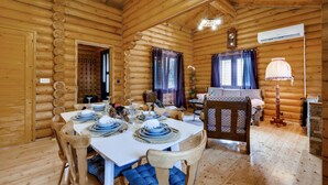 Interior acogedor de una cabaña de troncos con comedor listo para una comida, con paredes de madera, una mesa blanca y un reloj en la pared.