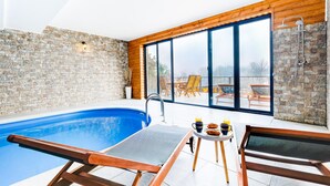 Un área de piscina interior moderna con vistas despejadas al exterior, suelo de madera y una mesa con alimentos para el desayuno.
