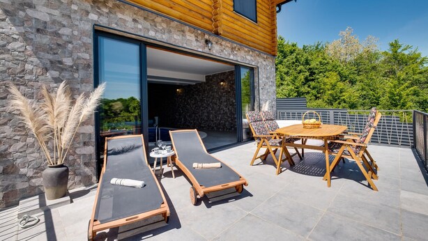 Un patio moderno al aire libre con sillones de descanso, una mesa y un muro de piedra.