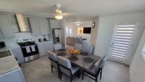 Une cuisine moderne avec un coin repas, comprenant un îlot central, des chaises à revêtement gris et un ventilateur de plafond.
