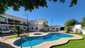 Une piscine à bord incurvé, entourée d’une pelouse bien entretenue et, au fond, un bâtiment avec un toit jaune.