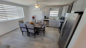 Une cuisine moderne dotée d’un coin repas, comprenant un îlot central, des appareils électroménagers intégrés et un ventilateur de plafond.