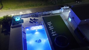 Une piscine extérieure dotée d’un éclairage bleu et entourée de chaises longues et d’une petite terrasse.