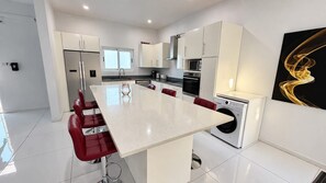 A modern kitchen with white cabinetry, a central island with seating, and a washing machine. - PÀRIS Villas 3BD Villa Rodney Bay (Gros Islet)